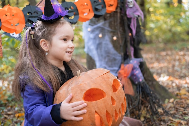 Víspera de Todos los Santos. linda niña disfrazada de bruja con calabaza divirtiéndose al aire libre