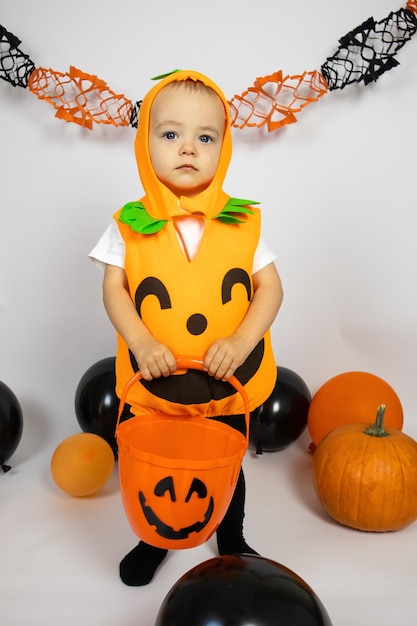 Víspera de Todos los Santos. Un niño pequeño disfrazado de calabaza se para con un cubo naranja