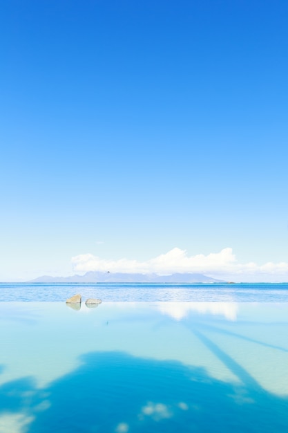 Vista à beira-mar piscina e céu azul na cena do dia ensolarado com sombra de palmeira na água,