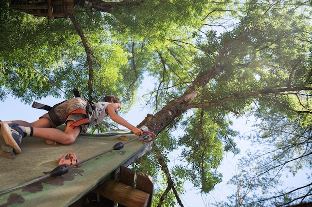 Vista desde abajo de un joven trepando por un muro de escalada en un árbol.