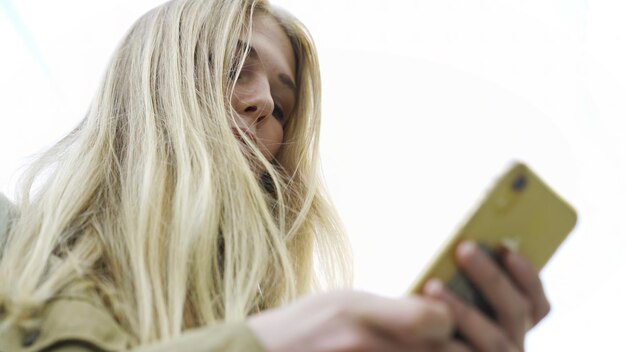 Foto vista de abajo de una mujer joven atractiva usando el teléfono al aire libre mujer de medios con cabello largo escribiendo texto