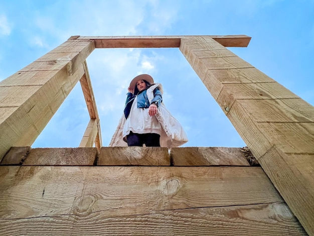 Vista desde abajo de una mujer con sombrero de pie sobre una estructura de madera