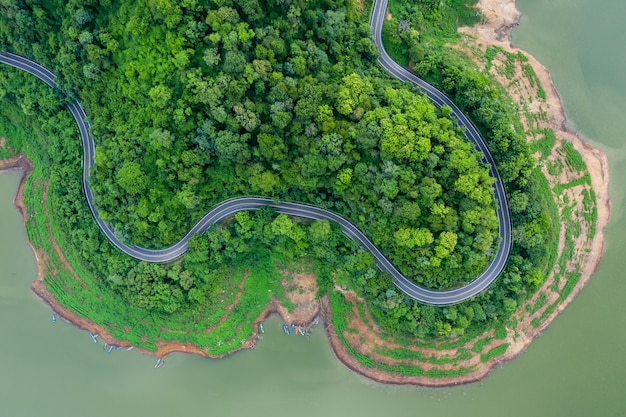 Vista aérea acima da floresta de montanha verde e rio na estação das chuvas e estrada curvada na colina que liga o campo