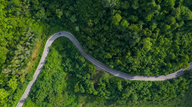 Vista aérea acima da floresta de montanha verde na estação das chuvas e estrada curva na colina conectando o campo