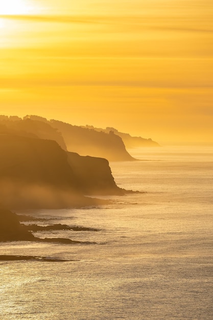 Vista aérea de algunos acantilados en el mar en una puesta de sol de colores naranjas y niebla sobre el agua Asturias España