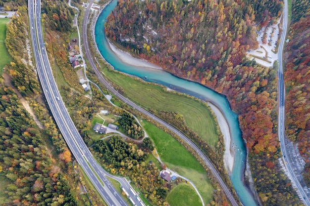 Vista aérea del amanecer superior de la carretera de velocidad de la autopista entre los árboles del bosque amarillo del otoño y el río azul.