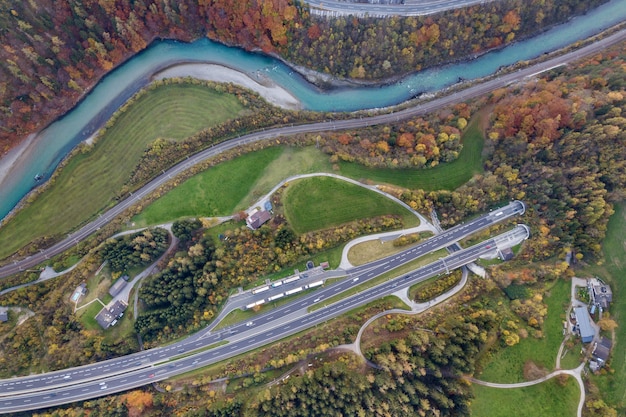 Vista aérea del amanecer superior de la carretera de velocidad de autopista que sale del túnel subterráneo entre los árboles del bosque amarillo del otoño y el río azul.