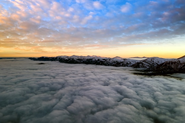 Vista aérea del amanecer vibrante sobre densas nubes blancas con montañas oscuras distantes en el horizonte.