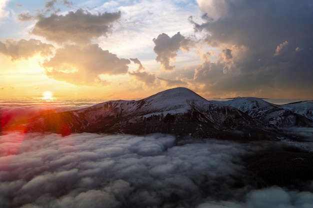 Vista aérea del amanecer vibrante sobre niebla densa blanca con montañas de los Cárpatos oscuros distantes en el horizonte.