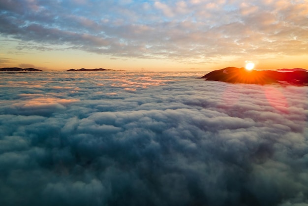 Vista aérea del amanecer vibrante sobre nubes densas blancas con montañas oscuras distantes en el horizonte