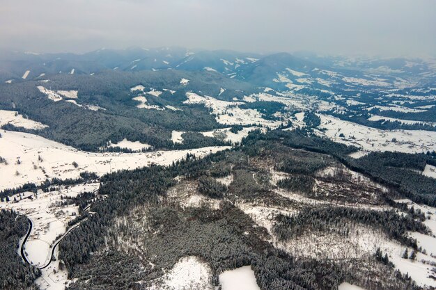 Vista aérea del árido paisaje invernal con colinas de montaña cubiertas de bosque de pinos de hoja perenne después de fuertes nevadas en la fría noche tranquila.