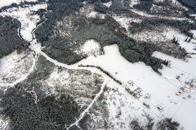 Vista aérea del árido paisaje invernal con colinas de montaña cubiertas de bosque de pinos de hoja perenne después de fuertes nevadas en la fría noche tranquila.