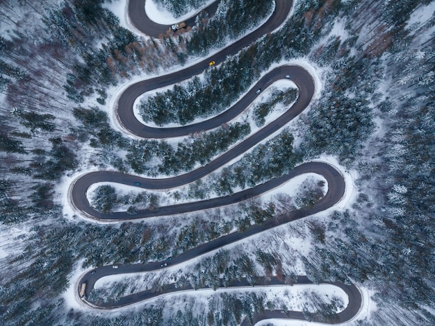 Vista aérea de arriba hacia abajo del camino sinuoso de invierno en el bosque Transilvania Rumania