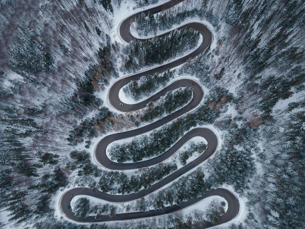 Vista aérea de arriba hacia abajo del camino sinuoso de invierno en el bosque Transilvania Rumania