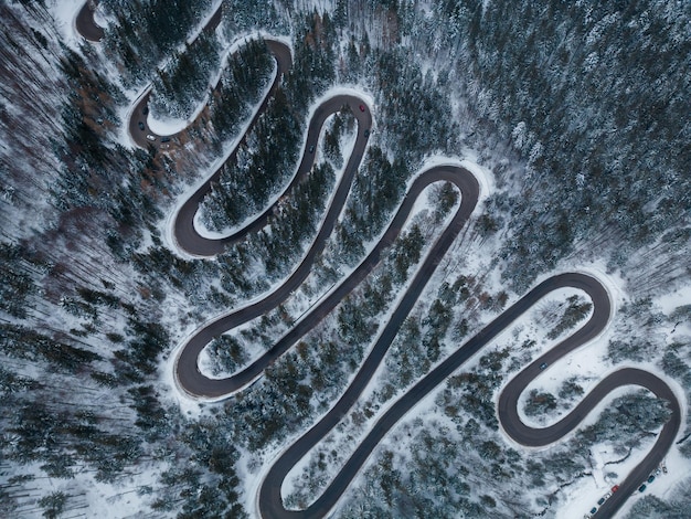Vista aérea de arriba hacia abajo del camino sinuoso de invierno en el bosque Transilvania Rumania