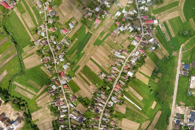 Vista aérea de arriba hacia abajo de la ciudad o pueblo con hileras de edificios y calles con curvas entre campos verdes en verano. Paisaje de campo desde arriba.