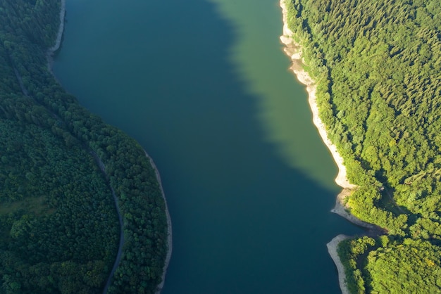 Vista aérea de arriba hacia abajo del gran lago con agua azul clara entre colinas de alta montaña cubiertas de un denso bosque siempre verde.