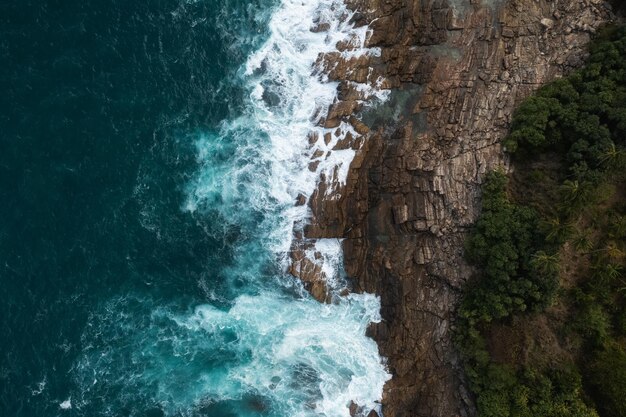 Vista aérea de arriba hacia abajo de la gran ola de la costa rompiendo en el acantilado de roca hermosa superficie oscura del mar en la soleada da