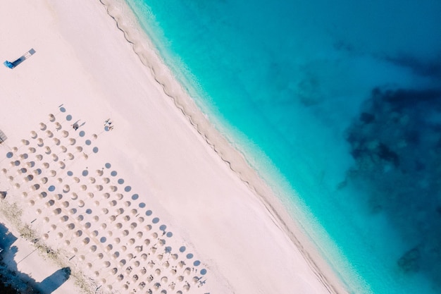 Vista aérea de arriba hacia abajo de una playa limpia equipada con sombrillas y tumbonas en el mar turquesa. Grecia.