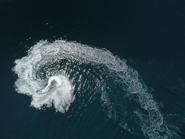 Vista aérea de arriba hacia abajo del rastro de espuma de agua con un agradable tono azul profundo del hermoso sendero blanco del océano en