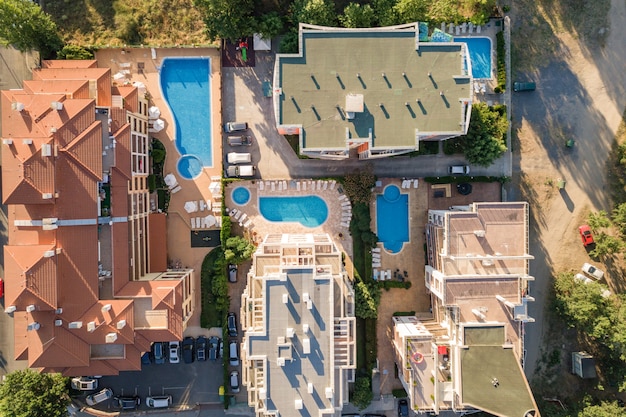 Vista aérea de arriba a abajo de los techos de los hoteles, calles con autos estacionados y piscinas con agua azul en una ciudad turística cerca del mar