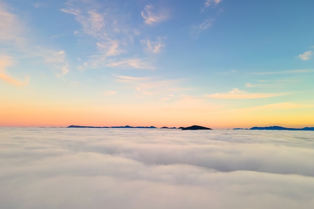 Vista aérea desde arriba de nubes blancas hinchadas al atardecer amarillo y montañas distantes.