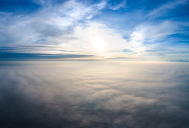 Vista aérea del atardecer amarillo sobre nubes blancas hinchadas con montañas distantes en el horizonte.