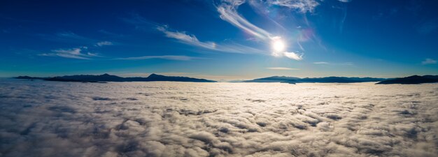 Vista aérea del atardecer amarillo sobre nubes blancas hinchadas con montañas distantes en el horizonte.