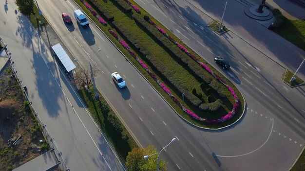 Vista aérea desde un avión no tripulado de coches que circulan por la carretera de la ciudad decorada con flores y un clip de césped verde