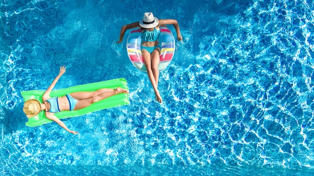 Vista aérea del avión no tripulado de los niños en la piscina desde arriba, los niños felices nadan en un anillo inflable con donas y colchones, las niñas se divierten en el agua en vacaciones familiares en el complejo vacacional