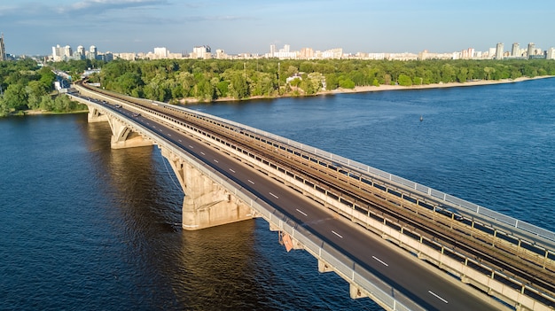 Vista aérea de aviones no tripulados del puente ferroviario de Metro con tren y río Dnieper. Horizonte de la ciudad de Kiev, Ucrania