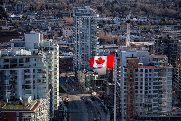 Vista aérea de una bandera canadiense ondeando al viento con edificios en segundo plano.