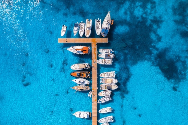 Vista aérea de barcos y yates de lujo en el muelle al atardecer en verano en Cerdeña Italia Paisaje colorido con veleros y lanchas en la bahía del mar jatty mar azul claro Vista superior del puerto Viajes