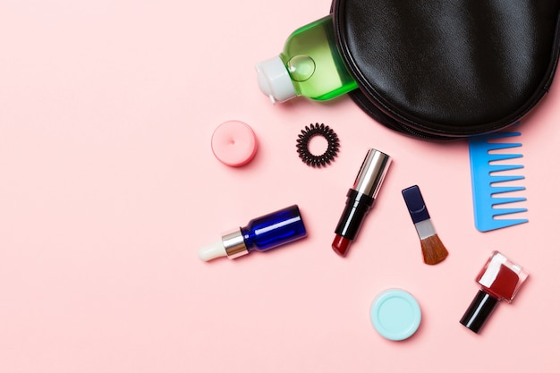 Vista aérea de una bolsa de cosméticos de cuero con productos de belleza de maquillaje derramándose en rosa