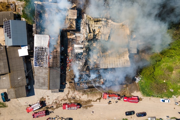 Vista aérea de los bomberos extinguiendo el edificio en ruinas en llamas con techo derrumbado y humo oscuro ascendente.