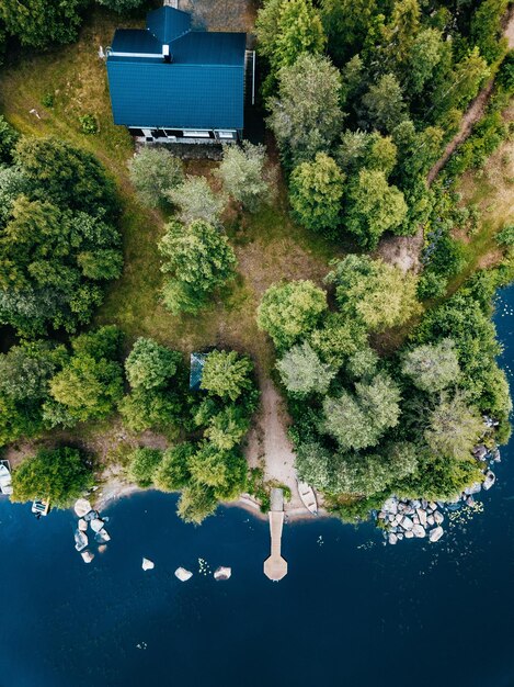 Vista aérea de una cabaña de madera en un bosque verde junto al lago azul en el verano rural de Finlandia