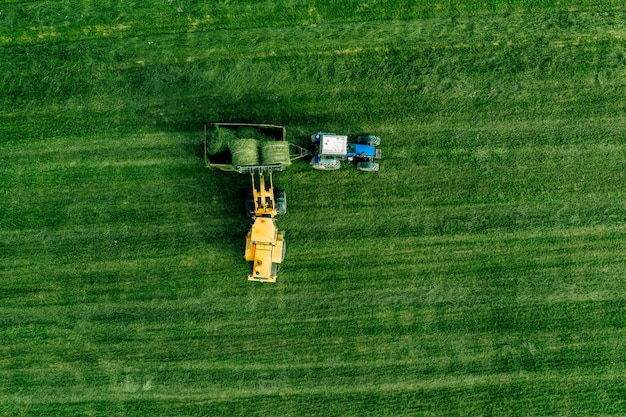 Vista aérea del campo de cosecha de hierba verde con tractor moviendo balas de heno en Finlandia