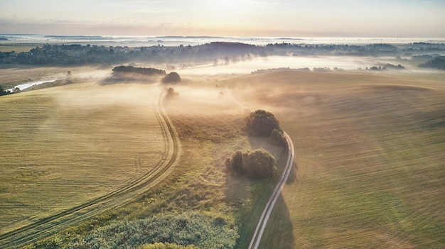 Vista aérea de un campo rural nublado con exuberantes campos verdes y una sinuosa carretera de tierra