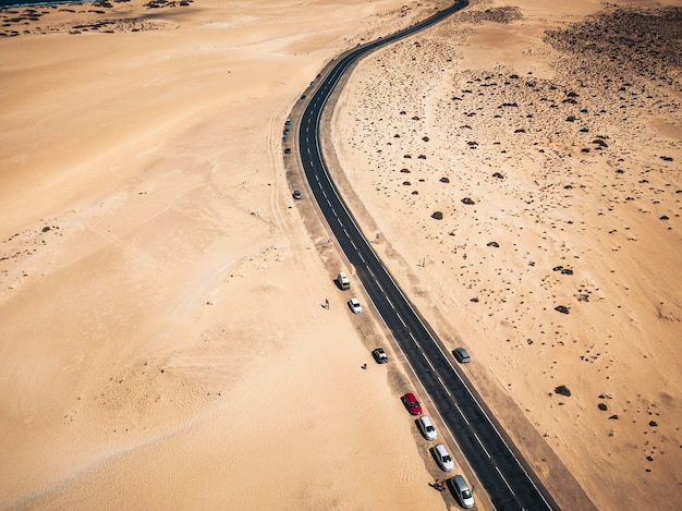 Vista aérea de la carretera de asfalto negro en medio de la playa - desierto alrededor y concepto de viajes y vacaciones. Lugar escénico tropical: transporte y automóviles estacionados en un paisaje salvaje