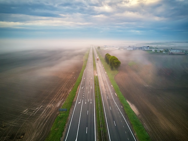 Vista aérea de una carretera cubierta por niebla. Temprano en la mañana brumosa. Carretera en campos de primavera verano. Autostrada en tiempo lluvioso. Bielorrusia, región de Minsk