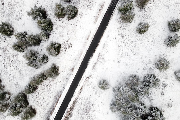 Vista aérea de la carretera cubierta de nieve vacía en el bosque de invierno.