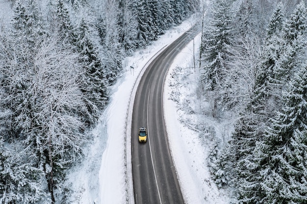 Vista aérea de la carretera de invierno con un coche y árboles cubiertos de nieve en el bosque de Finlandia