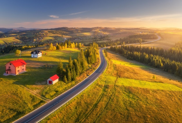 Vista aérea de la carretera de montaña en el pueblo al atardecer en otoño Vista superior desde el dron de la carretera en el bosque Hermoso paisaje con carretera bosque casas vacas prados verdes cielo colorido en otoño Viajes