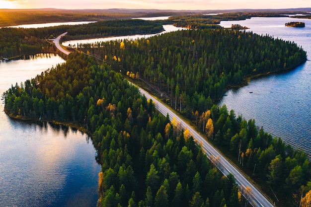 Vista aérea de la carretera rural en un bosque verde de verano con lagos azules al atardecer en Finlandia