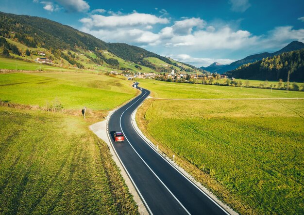 Foto vista aérea de la carretera en el valle de la montaña al atardecer en primavera en dolomitas italia vista superior de la carretera de asfalto colinas de automóviles con prados verdes cielo azul árboles edificios carretera y campos naturaleza