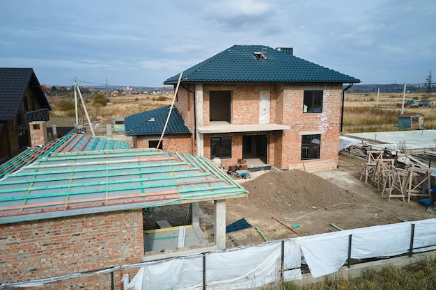 Vista aérea de una casa inacabada con paredes de ladrillo y techo de madera cubierto con tejas metálicas en construcción