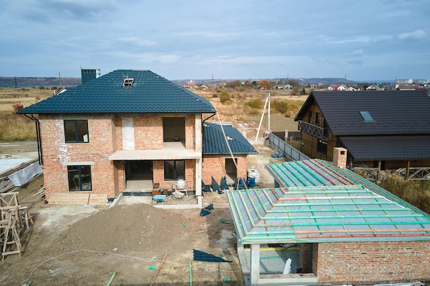 Vista aérea de una casa inacabada con paredes de ladrillo y techo de madera cubierto con tejas metálicas en construcción