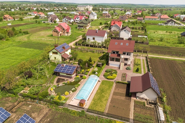 Vista aérea de una casa privada en verano con paneles fotovoltaicos solares azules en la azotea y en el patio.