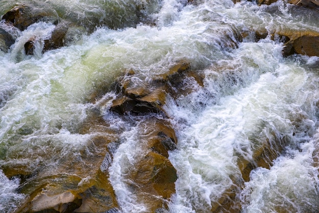 Vista aérea de la cascada del río con agua turquesa clara cayendo entre rocas mojadas con espuma blanca espesa.