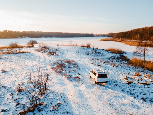 Vista aérea del coche todoterreno en la playa del lago congelado en el espacio de copia al atardecer